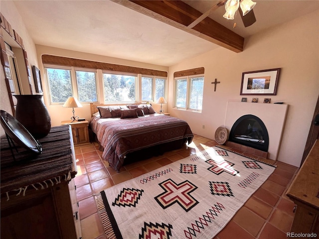 bedroom featuring a glass covered fireplace, light tile patterned flooring, and beamed ceiling