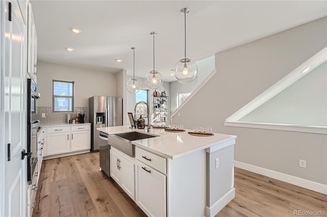 kitchen with sink, stainless steel appliances, white cabinets, an island with sink, and pendant lighting