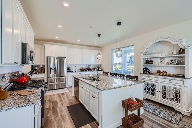 kitchen featuring sink, appliances with stainless steel finishes, light stone countertops, an island with sink, and white cabinets