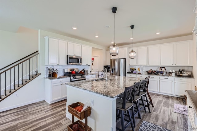 kitchen featuring decorative light fixtures, sink, dark stone countertops, a kitchen island with sink, and stainless steel appliances