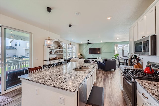 kitchen with decorative light fixtures, an island with sink, white cabinetry, sink, and stainless steel appliances