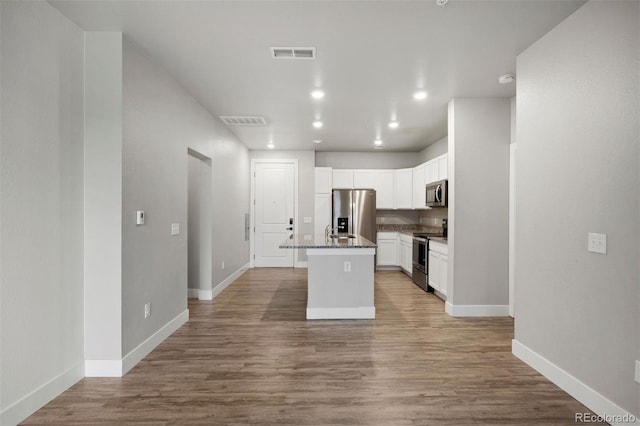 kitchen featuring stainless steel appliances, baseboards, white cabinetry, wood finished floors, and an island with sink