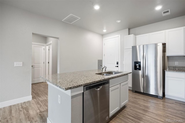 kitchen with stainless steel appliances, a sink, light stone counters, white cabinetry, and light wood-style floors