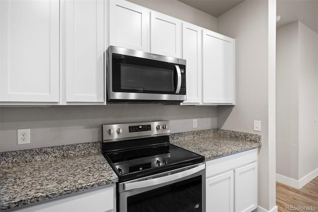 kitchen featuring stainless steel appliances, white cabinets, stone counters, and baseboards