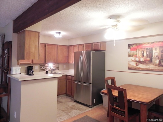 kitchen featuring sink, a textured ceiling, stainless steel fridge, kitchen peninsula, and ceiling fan