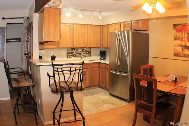 kitchen with sink, stainless steel refrigerator, ceiling fan, backsplash, and light hardwood / wood-style floors