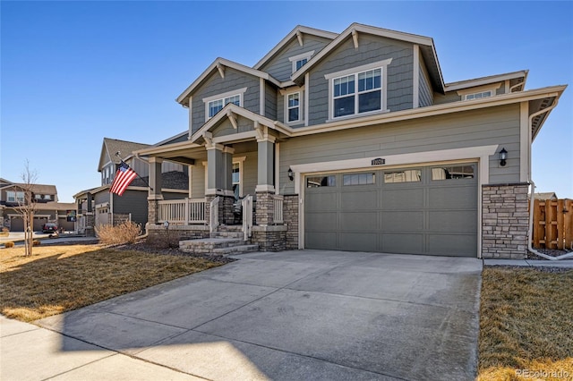 craftsman-style home with fence, driveway, an attached garage, covered porch, and stone siding