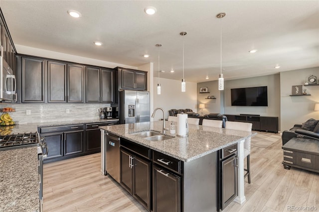 kitchen with a sink, light stone counters, open floor plan, stainless steel appliances, and decorative backsplash