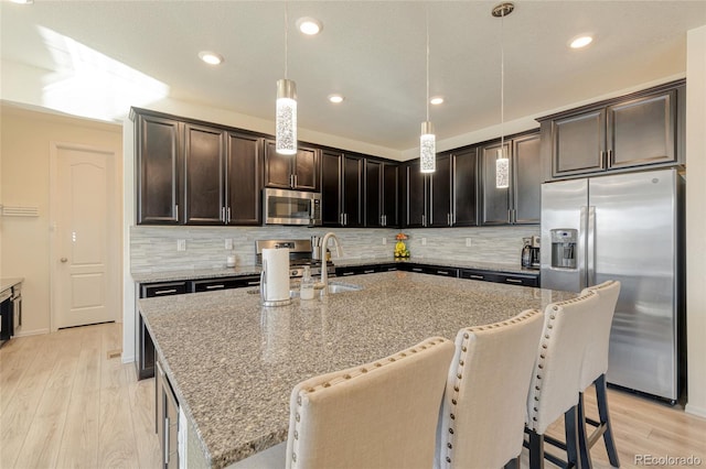 kitchen featuring light wood-type flooring, stainless steel appliances, light stone counters, and tasteful backsplash