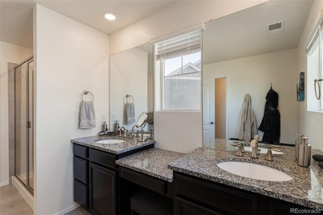 full bath with visible vents, a stall shower, two vanities, and a sink