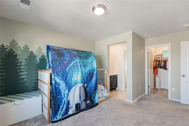 carpeted bedroom featuring visible vents, a textured ceiling, a walk in closet, and baseboards