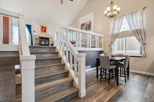 stairs with hardwood / wood-style flooring, a notable chandelier, and high vaulted ceiling