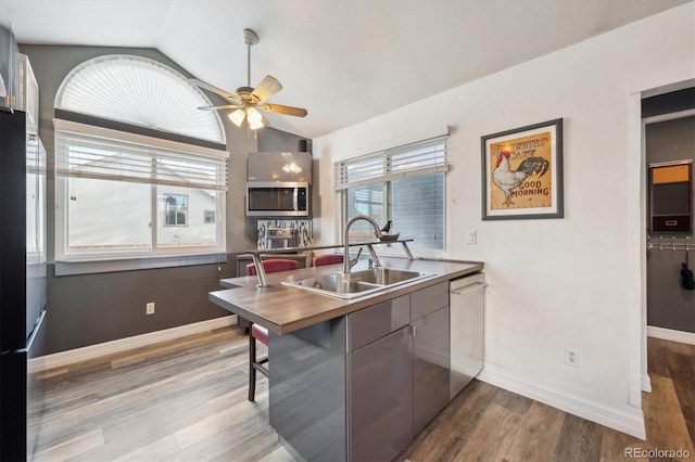 kitchen with appliances with stainless steel finishes, ceiling fan, sink, light hardwood / wood-style floors, and lofted ceiling