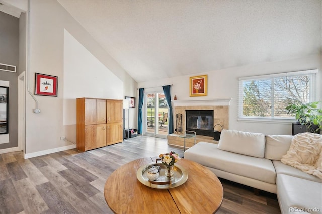 living room featuring a textured ceiling, light hardwood / wood-style flooring, vaulted ceiling, and a tiled fireplace