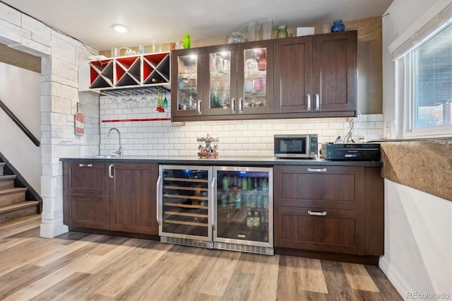 bar featuring dark brown cabinetry, backsplash, light hardwood / wood-style flooring, and beverage cooler