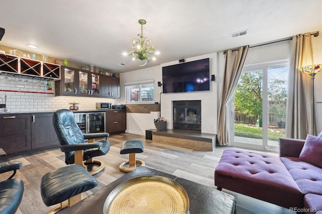 living room featuring an inviting chandelier, light wood-type flooring, and indoor bar