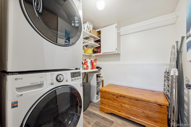 laundry room featuring stacked washing maching and dryer and light hardwood / wood-style flooring