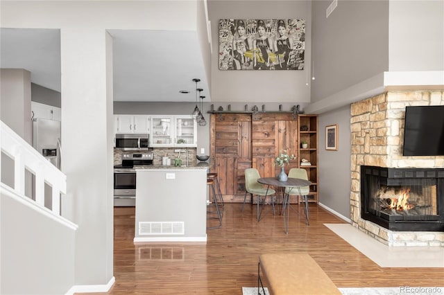 6858 Zenobia St Unit 9, Westminster, CO 80030 - kitchen featuring appliances with stainless steel finishes, a towering ceiling, white cabinetry, wood finished floors, and a stone fireplace