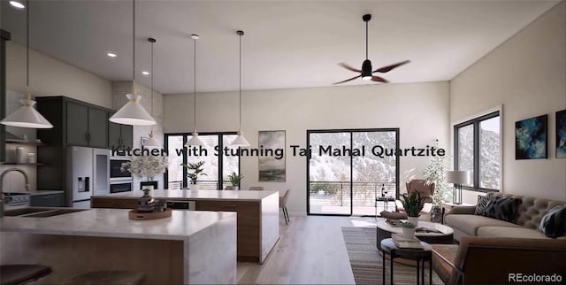 kitchen featuring appliances with stainless steel finishes, hanging light fixtures, a high ceiling, a kitchen island, and light wood-type flooring