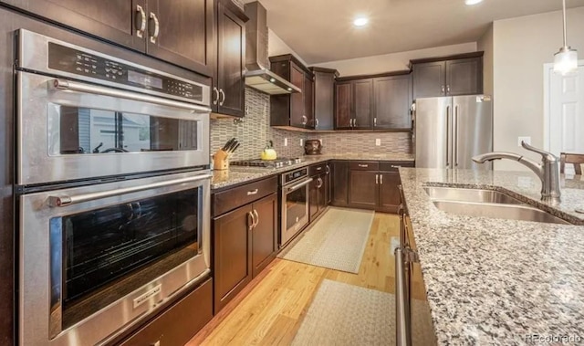 6765 Windbrook Ct, Colorado Springs, CO 80927 - kitchen with appliances with stainless steel finishes, wall chimney exhaust hood, light wood-type flooring, dark brown cabinetry, and light stone counters