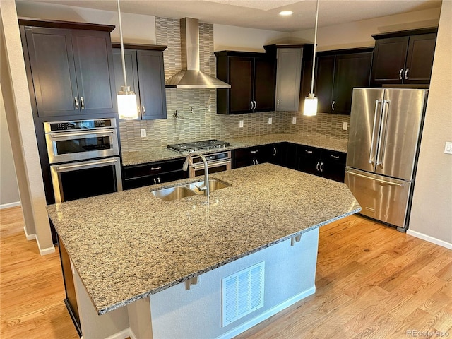 6765 Windbrook Ct, Colorado Springs, CO 80927 - kitchen with stainless steel appliances, wall chimney range hood, decorative backsplash, light stone counters, and a center island with sink