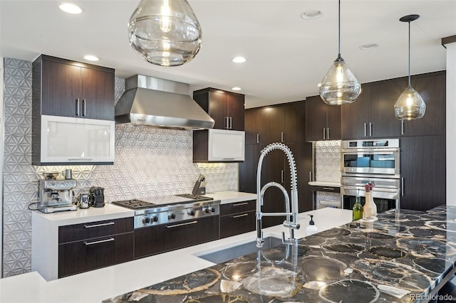 621 Kearney St, Denver, CO 80220 - kitchen with decorative backsplash, dark brown cabinets, wall chimney range hood, hanging light fixtures, and stainless steel appliances