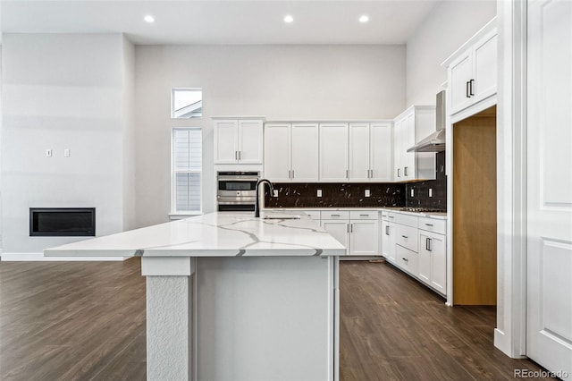 kitchen featuring white cabinets, dark hardwood / wood-style floors, light stone countertops, an island with sink, and tasteful backsplash