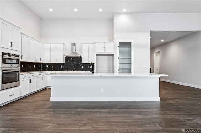 kitchen with white cabinetry, wall chimney exhaust hood, an island with sink, and dark hardwood / wood-style floors