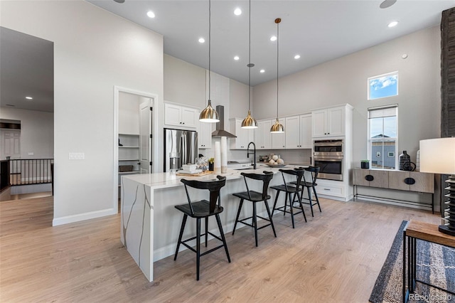 kitchen with pendant lighting, a kitchen island with sink, white cabinets, a towering ceiling, and stainless steel appliances