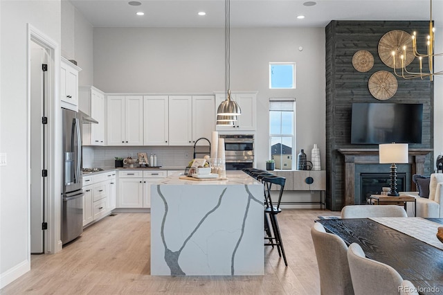 kitchen with hanging light fixtures, a high ceiling, light stone counters, a kitchen island with sink, and a fireplace