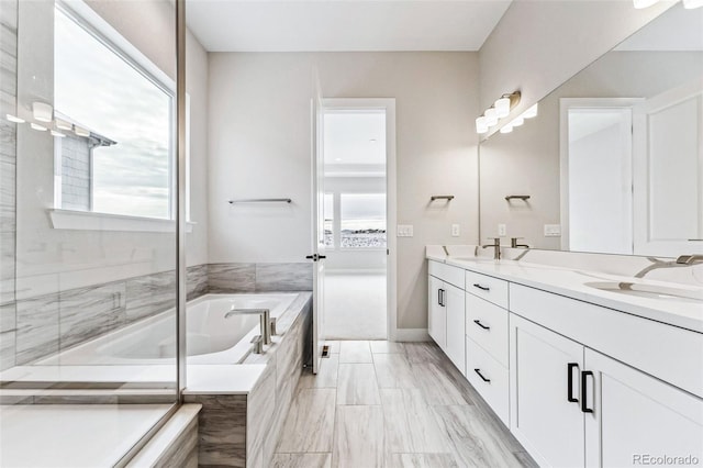 bathroom with vanity, a healthy amount of sunlight, and tiled tub