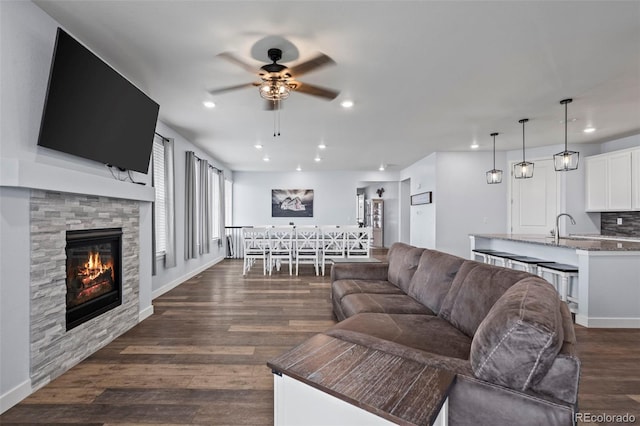 15604 Xenia Way, Brighton, CO 80602 - living area with ceiling fan, a stone fireplace, dark wood finished floors, recessed lighting, and baseboards