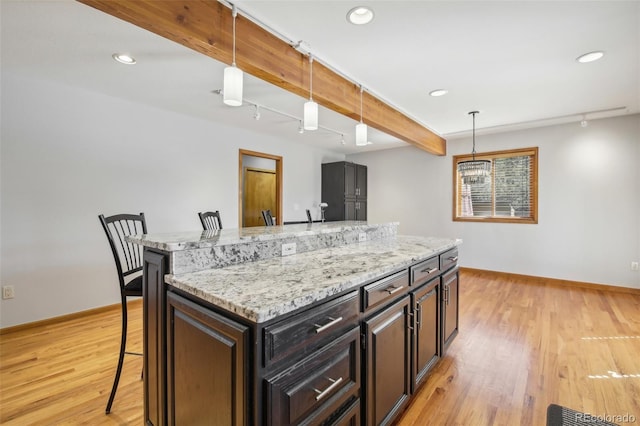 kitchen featuring hanging light fixtures, light hardwood / wood-style floors, a kitchen island, a kitchen bar, and dark brown cabinets