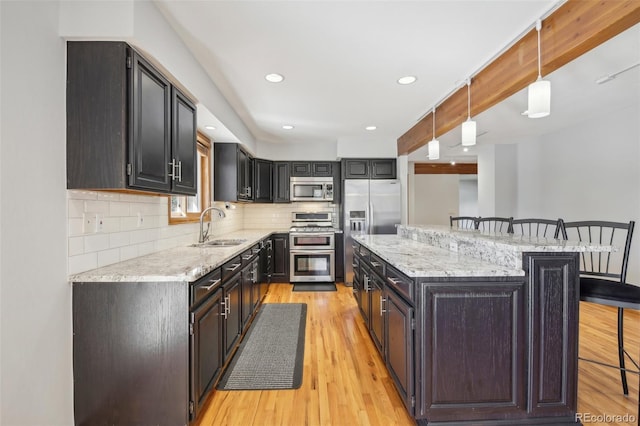 kitchen with a breakfast bar, pendant lighting, stainless steel appliances, light hardwood / wood-style flooring, and sink