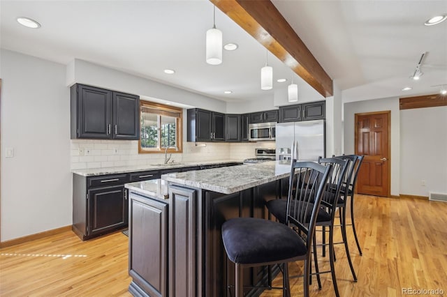 kitchen with appliances with stainless steel finishes, light wood-type flooring, a center island, and pendant lighting