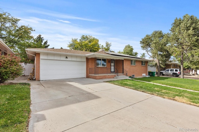 ranch-style home featuring concrete driveway, solar panels, an attached garage, a front lawn, and brick siding