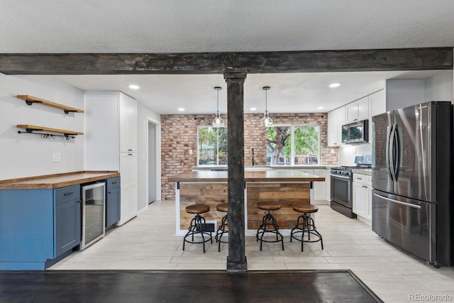 kitchen with white cabinets, beverage cooler, appliances with stainless steel finishes, wooden counters, and blue cabinets