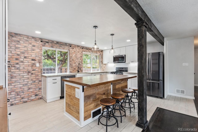 kitchen with light hardwood / wood-style flooring, stainless steel appliances, brick wall, pendant lighting, and white cabinets