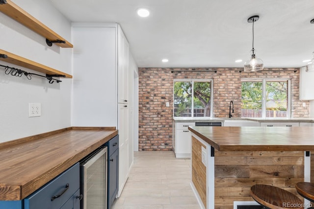 kitchen featuring beverage cooler, sink, decorative light fixtures, blue cabinets, and brick wall