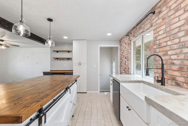 kitchen with sink, dishwasher, butcher block countertops, white cabinets, and brick wall