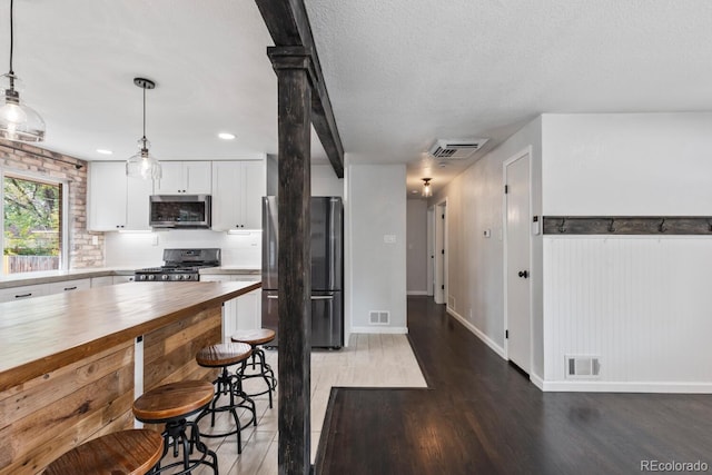 kitchen featuring dark hardwood / wood-style flooring, appliances with stainless steel finishes, white cabinetry, a textured ceiling, and pendant lighting