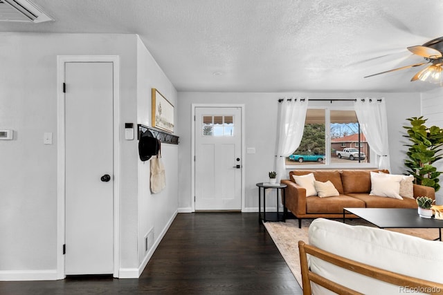 living room featuring a textured ceiling, visible vents, a ceiling fan, baseboards, and dark wood-style floors