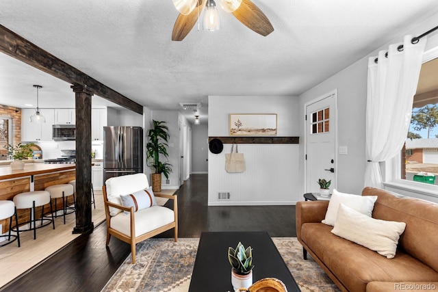 living room with dark wood finished floors, decorative columns, visible vents, a textured ceiling, and beamed ceiling