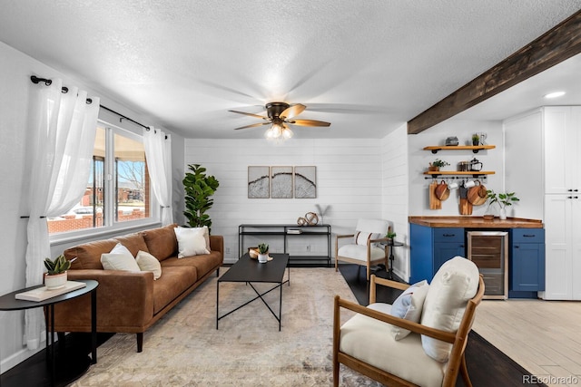 living area with a textured ceiling, wine cooler, a dry bar, light wood finished floors, and beamed ceiling