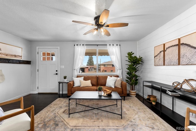 living room with ceiling fan, a textured ceiling, wood finished floors, and baseboards