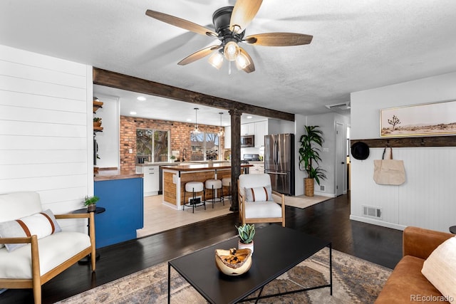 living area with a textured ceiling, ceiling fan, visible vents, light wood-style floors, and beam ceiling