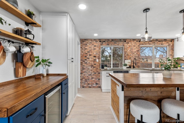 kitchen featuring a sink, wood counters, brick wall, blue cabinets, and beverage cooler