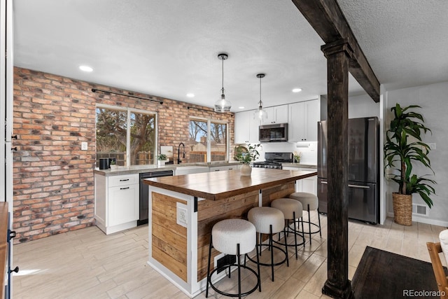 kitchen with appliances with stainless steel finishes, a textured ceiling, light wood-style floors, a kitchen bar, and wooden counters