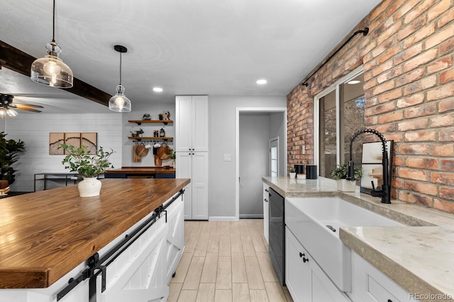 kitchen featuring black dishwasher, brick wall, butcher block counters, white cabinetry, and a sink