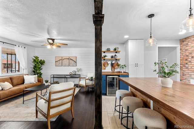 interior space with wine cooler, light wood-style flooring, a ceiling fan, a textured ceiling, and a bar